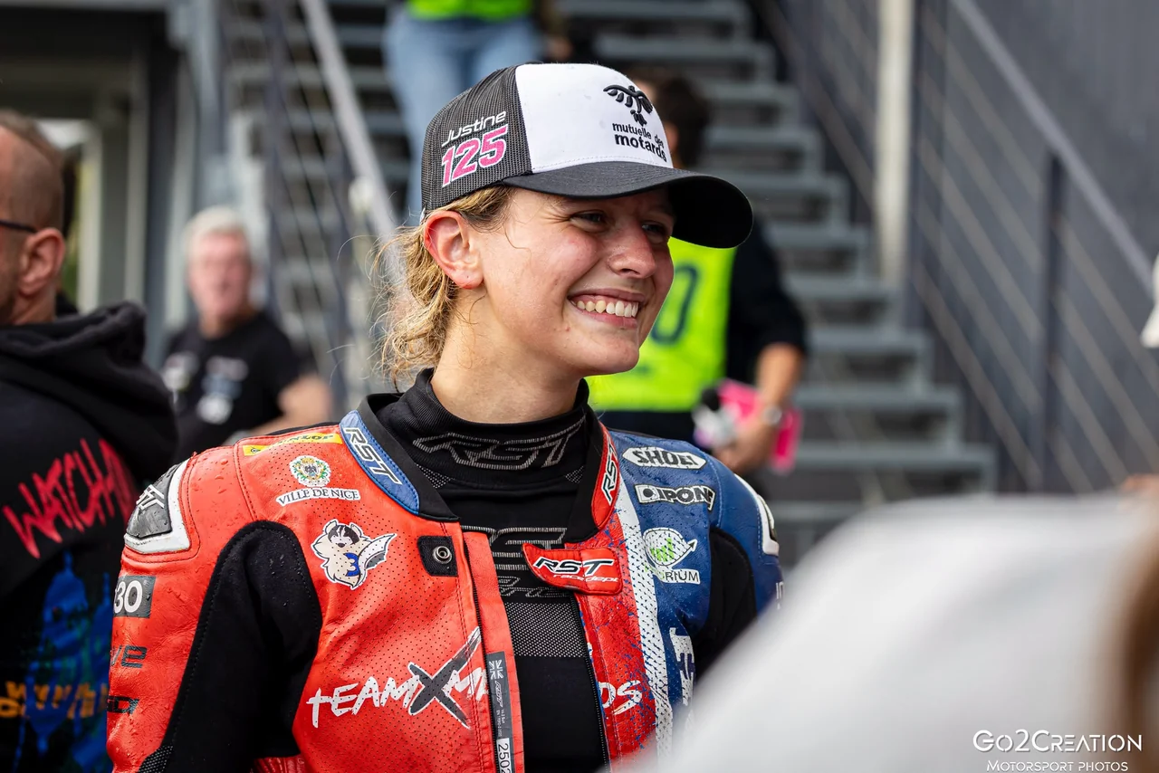 Justine souriante dans le paddock, en combinaison de course.